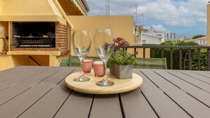 Een houten tafel met twee wijnglazen en twee roze kaarsen op een balkon, inclusief een bakoven en een bloempot.