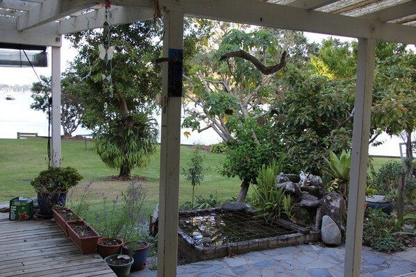 A covered patio area with a garden, a small pond, and a view of the water.
