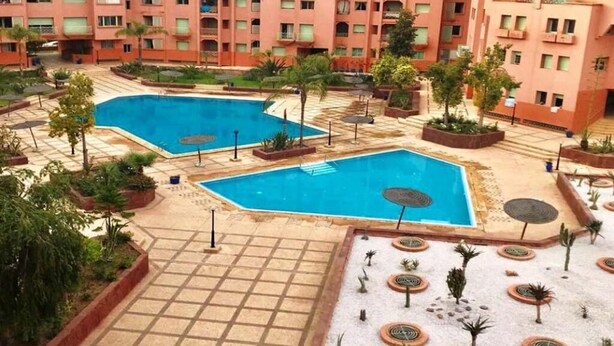 Un cortile d'hotel con due piscine, circondato da palme e un edificio di grandi dimensioni con balconi.