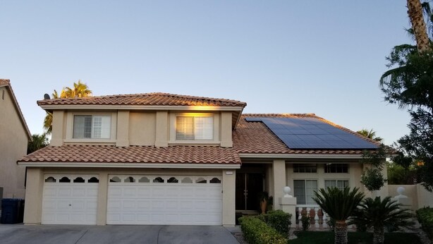 A two-story house with a tiled roof, solar panels, a garage, and a well-maintained lawn with palm trees.