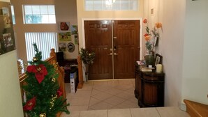 A hallway with a wooden door, a Christmas tree, and a vase with flowers.