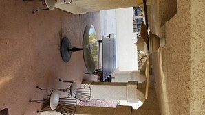 An outdoor patio with a round table and chairs, a large umbrella, and a view of a mountainous landscape.