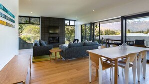 Una sala moderna con chimenea, un conjunto de sofás, una mesa de comedor y ventanas amplias que ofrecen vistas a la montaña.