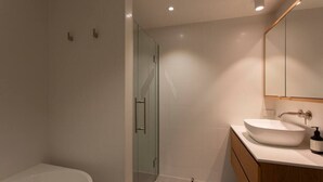 Un baño moderno con cabina de ducha de vidrio, un lavabo blanco y un mueble de tocador de madera.