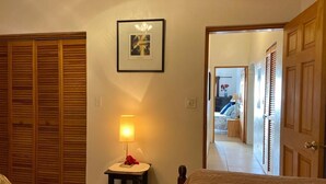 A bedroom with a bed, a bedside table with a lamp, a framed picture on the wall, and a wooden closet. - Blue Diamond Apartments (Warwick Parish)