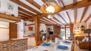 A rustic dining area with a long table set for a meal, wooden beams on the ceiling, and a brick wall. - Marguerite by Interhome (Capbreton)