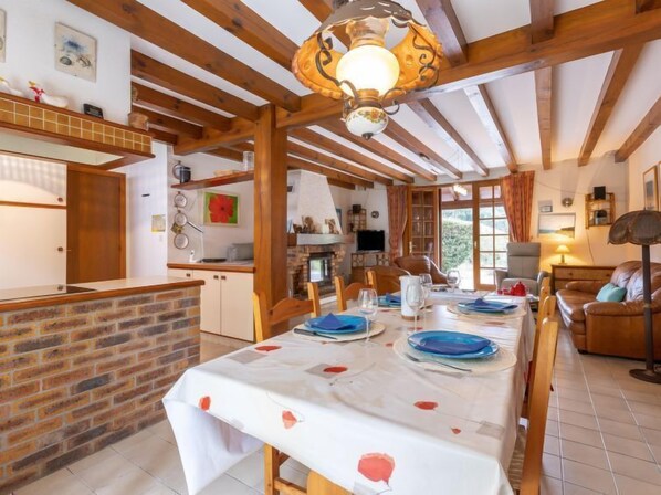 A rustic dining area with a long table set for a meal, wooden beams on the ceiling, and a brick wall.
