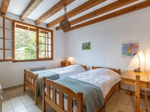 A bedroom with two wooden beds, a window with a view of greenery, a desk with a lamp, and a map on the wall.