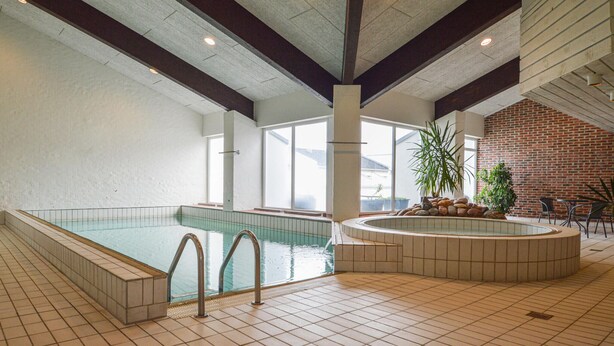 A large indoor swimming pool with multiple entry points, a brick wall, and a seating area with chairs and a table. - Feriehotal Tranum Klit (Brovst)