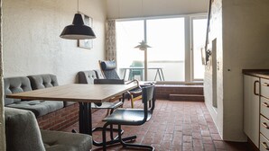 A dining area with a wooden table and chairs, a sofa, and a brick wall. - Feriehotal Tranum Klit (Brovst)