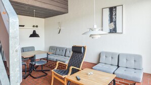 A modern interior with a brick floor, grey upholstered seating, a wooden table, and pendant lighting. - Feriehotal Tranum Klit (Brovst)