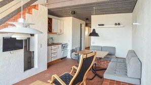 A modern kitchen with white cabinets, a dining area with a wooden table and chairs, and a grey sofa. - Feriehotal Tranum Klit (Brovst)