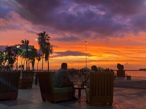 A sunset view with palm trees and people sitting on chairs. - Mechudo Brewinn (La Paz)