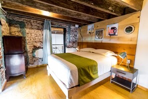 A bedroom with a wooden bed, a nightstand with a lamp, a dresser, and a brick wall. - Mechudo Brewinn (La Paz)
