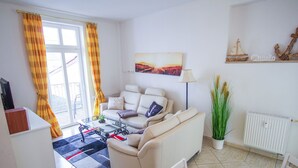Una sala de estar con sofá, mesa de centro, lámpara, radiador y ventana con cortinas.