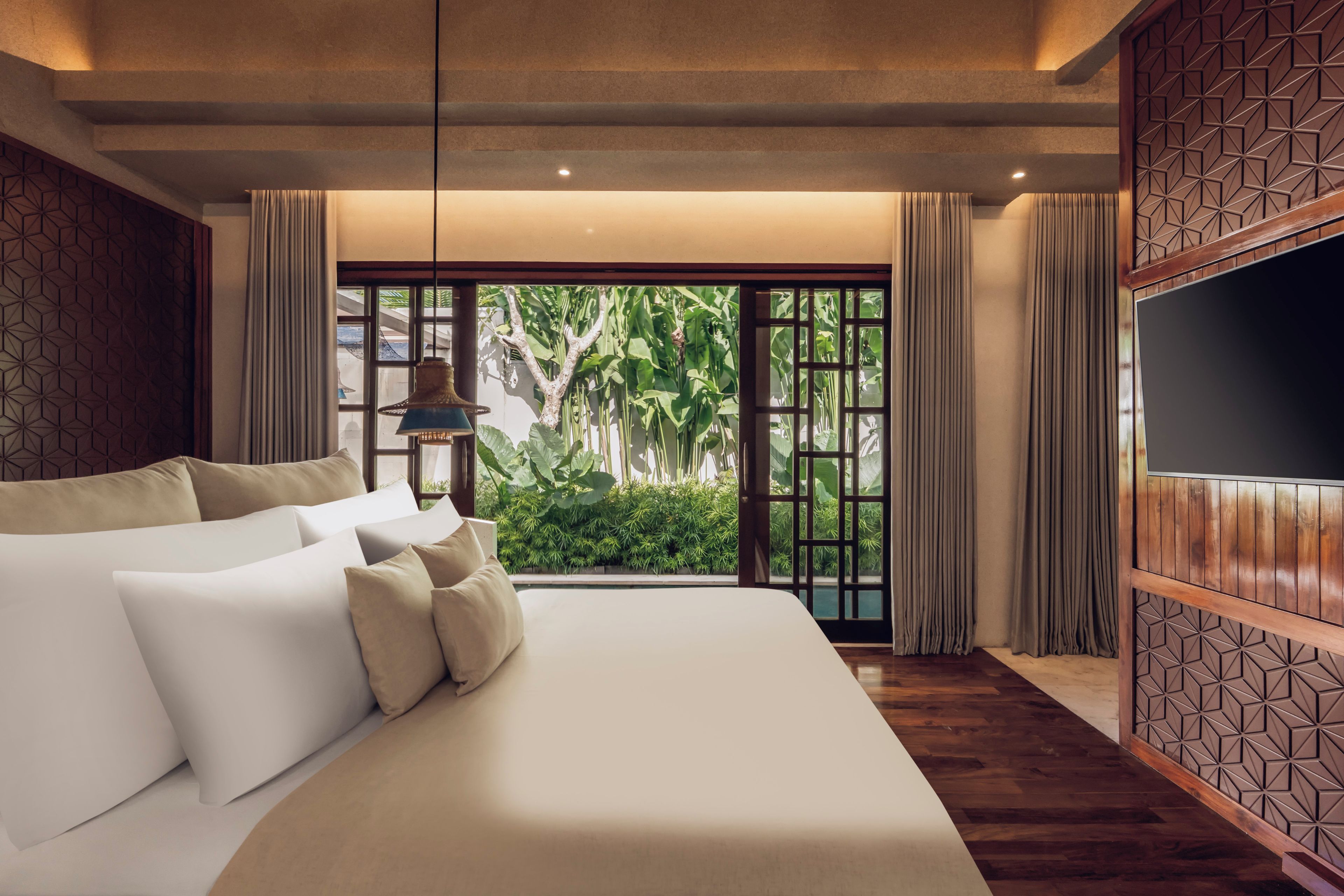 A hotel room with a large bed, a TV, and a view of greenery through the window.