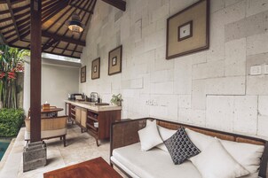 Uma cozinha moderna com bancada de madeira, pia embutida, um banco de madeira e um sofá branco com almofadas estampadas.
