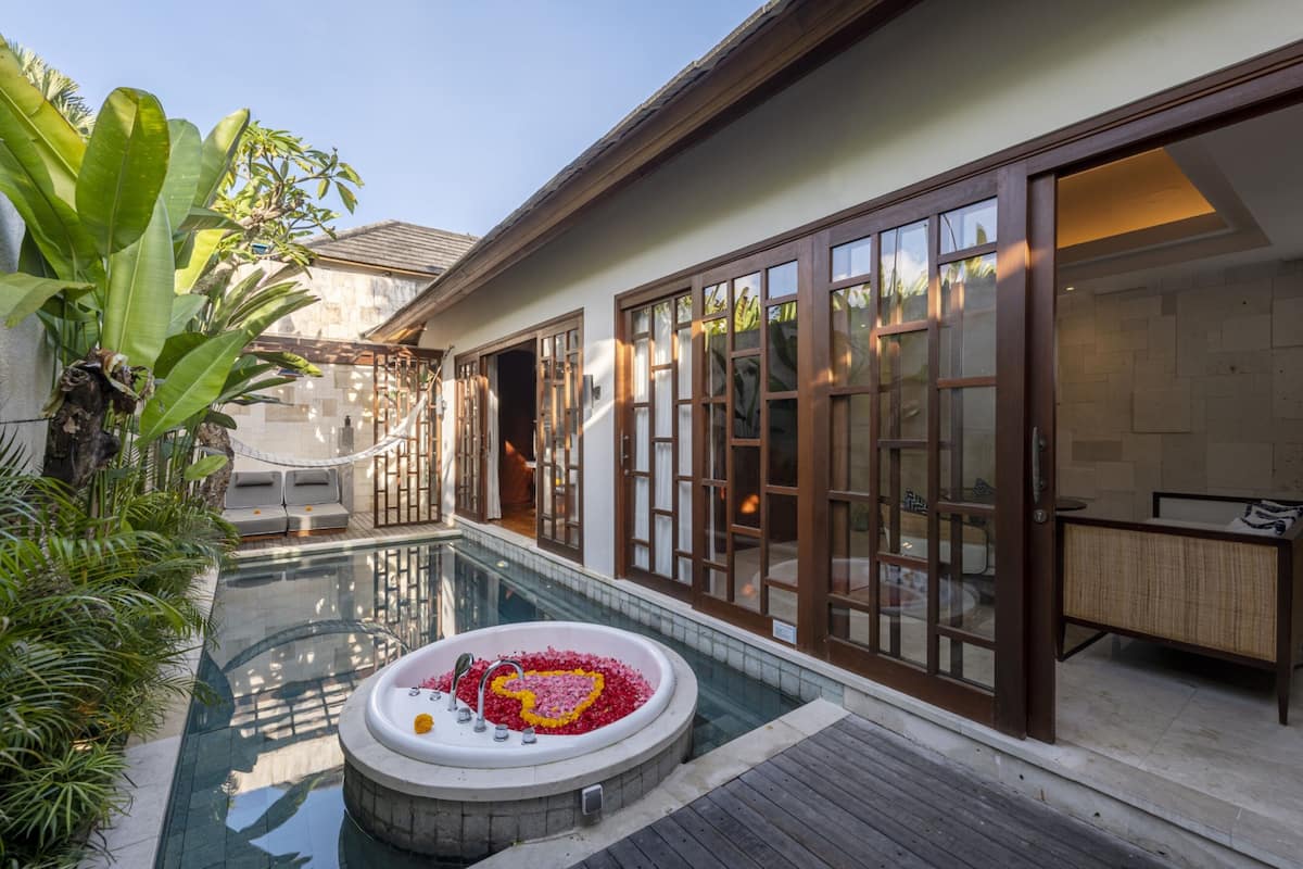 Ein Wellnessbereich mit Whirlpool, umgeben von einem Pool, einer Holzterrasse und einem großen Fenster mit Blick ins Innere.