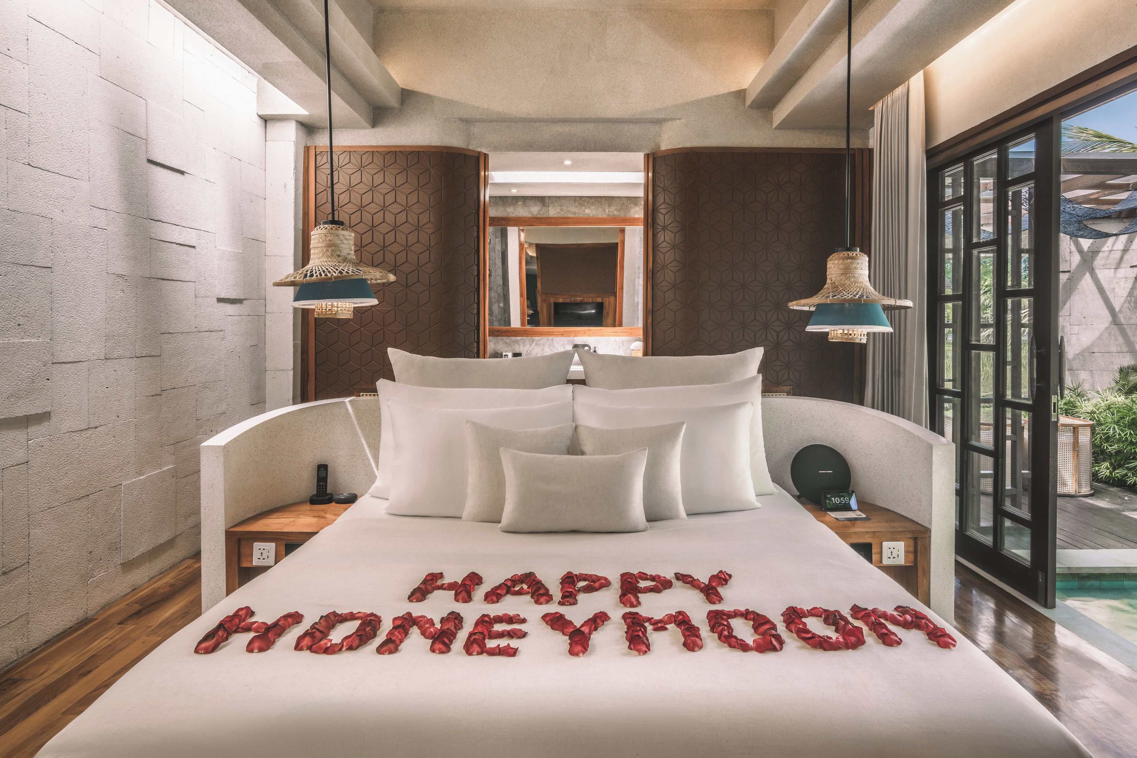 A hotel room with a bed, pillows, a bedside table with a phone, a nightstand, and a large window.