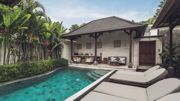 A poolside area with lounge chairs, a covered seating area, and lush tropical plants.