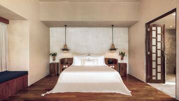 A spacious bedroom with a large bed, two bedside tables, a nightstand, a wooden bench, and a door leading to a bathroom.