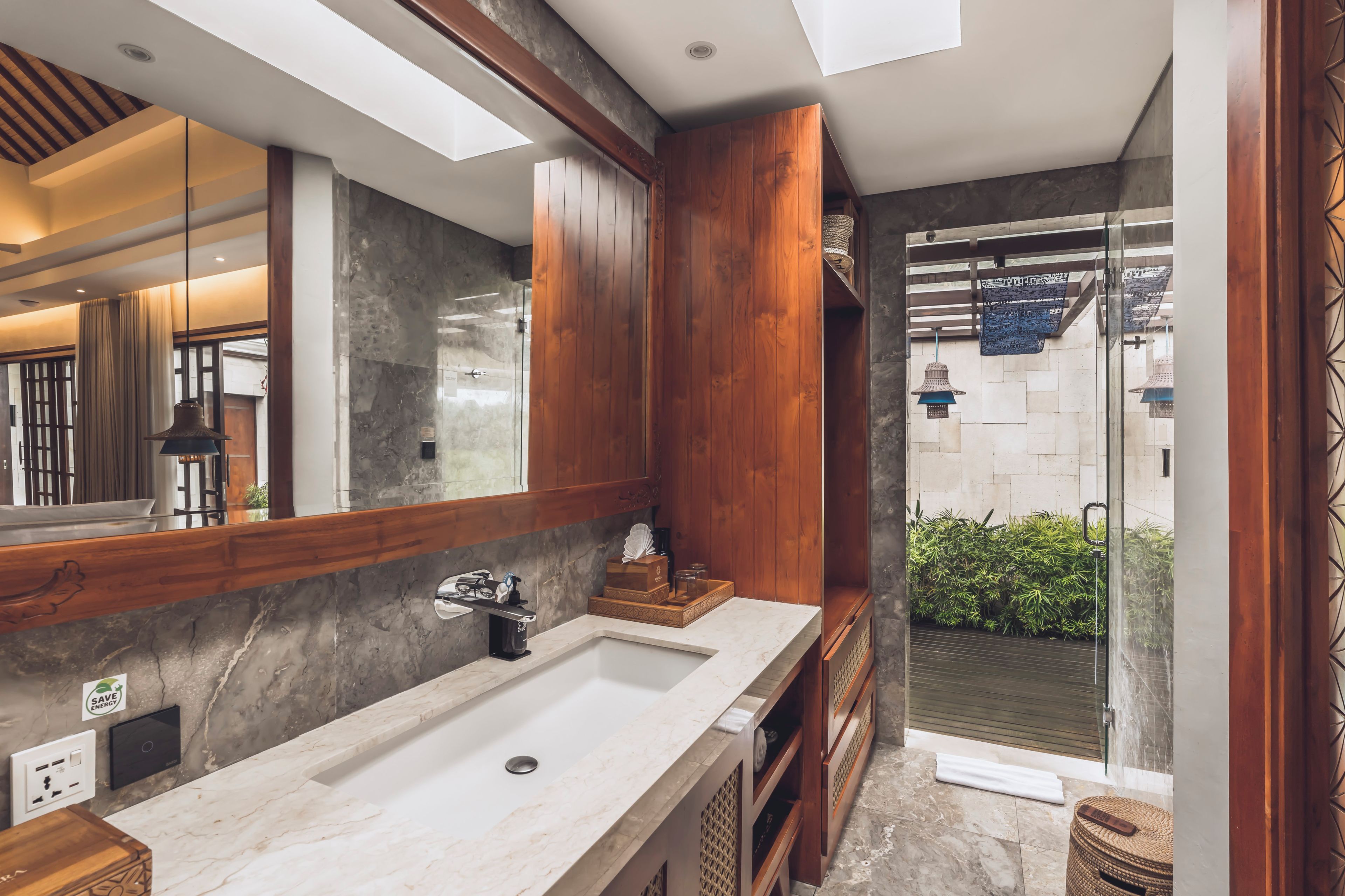 A modern bathroom with a large mirror, wooden cabinets, a marble sink, and a glass shower enclosure.