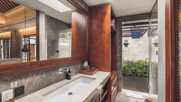 A modern bathroom with a large mirror, wooden cabinets, a marble sink, and a glass shower enclosure.