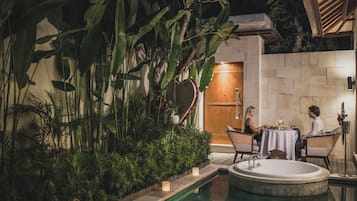 Un área de piscina con un jacuzzi, rodeada de exuberante follaje y un muro de piedra.