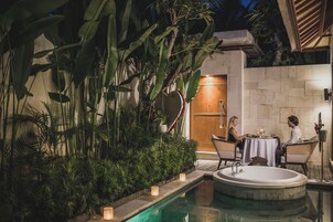 Área de piscina com hidromassagem, cercada por vegetação exuberante e uma parede de pedra.
