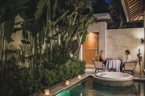 Un área de piscina con un jacuzzi, rodeada de exuberante follaje y un muro de piedra.
