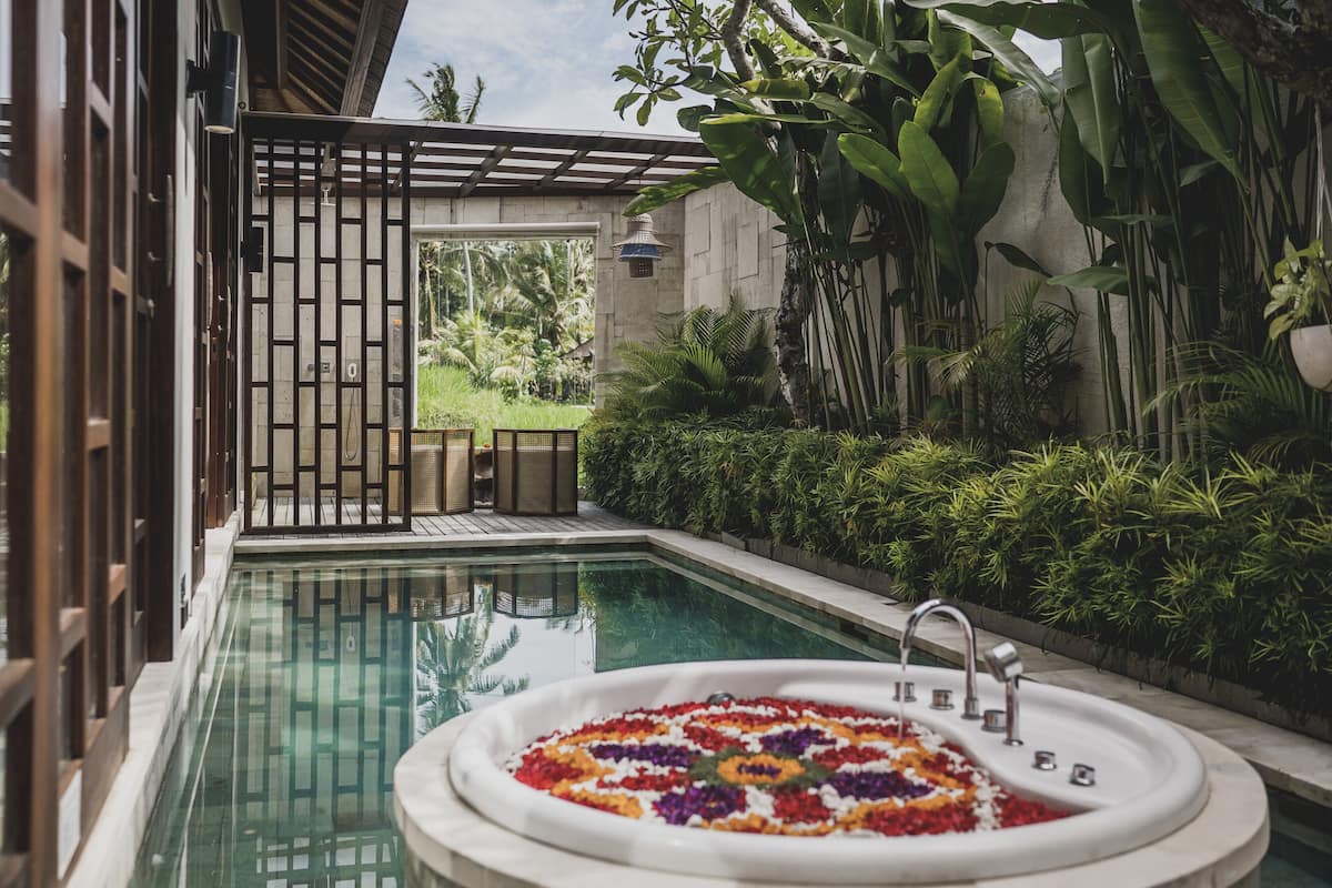 Ein Pool mit einer dekorativen Blumenanordnung in der Mitte, umgeben von üppigem Grün und einer Pergola.