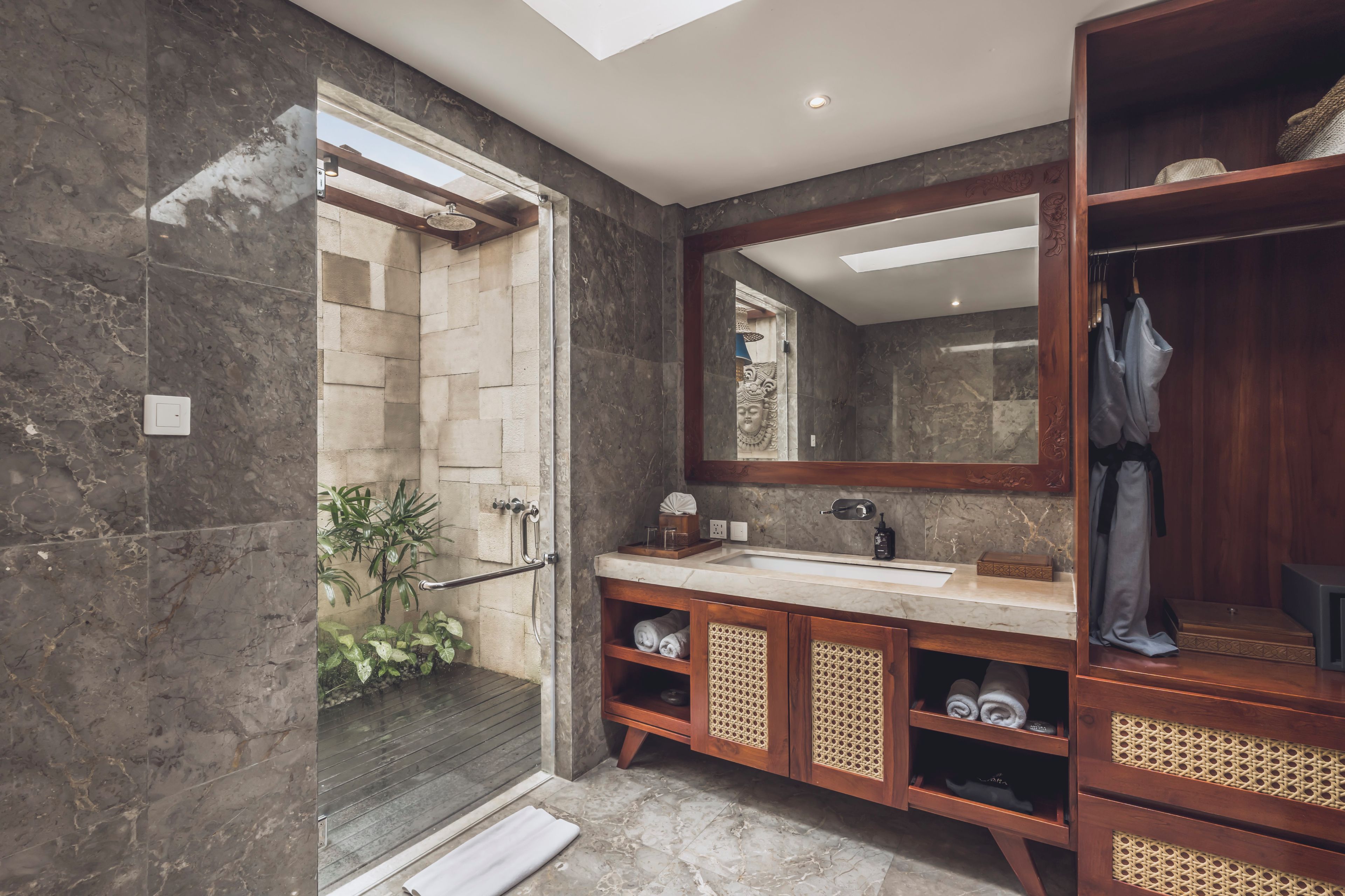 A modern bathroom with a glass shower enclosure, marble flooring, a wooden vanity with a large mirror, and a built-in wardrobe.