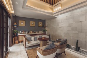 Una sala de estar moderna con un sofá, dos sillones, una mesita de centro y una zona de bar con electrodomésticos.