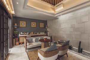 A modern living room with a sofa, two armchairs, a coffee table, and a bar area with kitchen appliances.