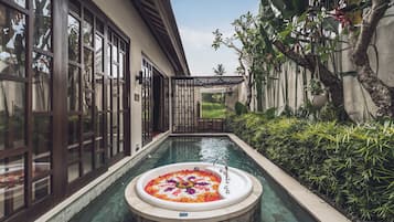 Una piscina con idromassaggio circondata da vegetazione lussureggiante e un edificio con ampie finestre.