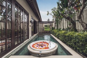 A pool with a jacuzzi surrounded by lush greenery and a building with large windows.