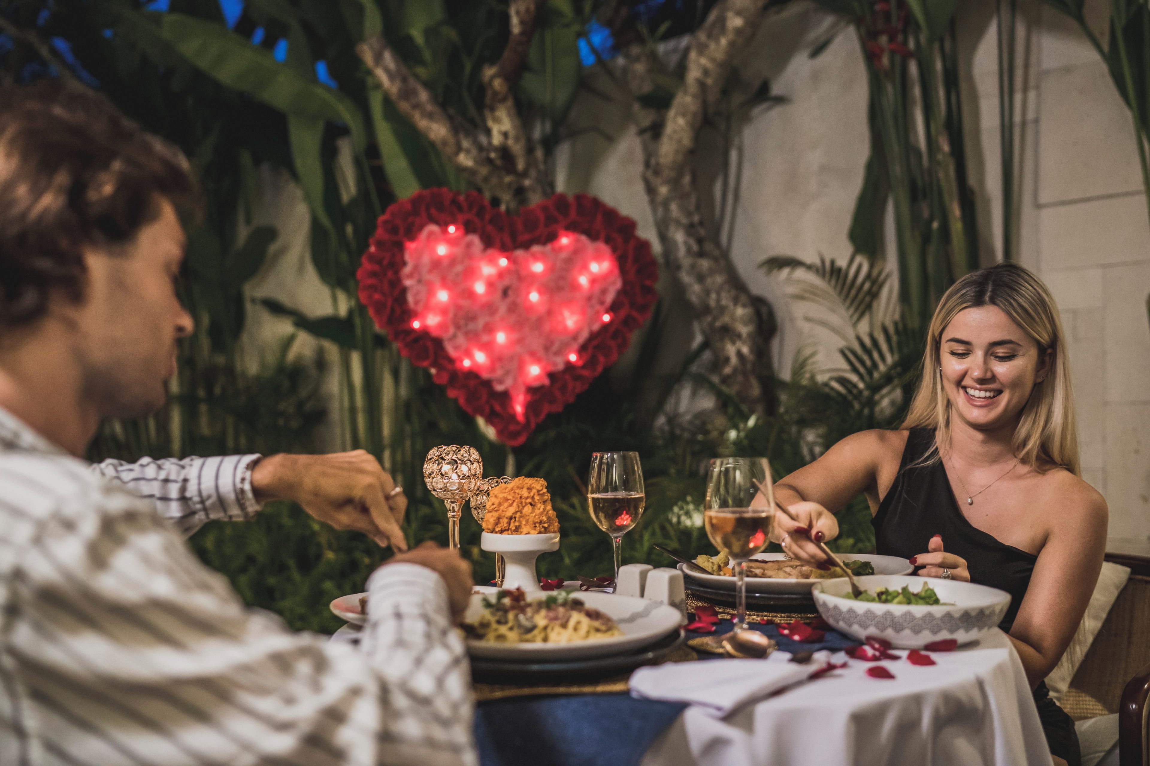 A couple dining at a table with a heart-shaped balloon, surrounded by greenery.