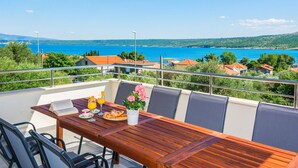 A balcony with a wooden table set for breakfast, overlooking a coastal landscape with houses and a clear blue sea. - Nice home in Posedarje with sauna (Posedarje)