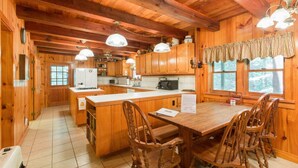 Interior de una cabaña de madera con cocina, comedor y ventanas amplias.