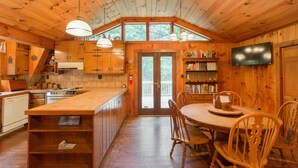 Interior de una cabaña de madera con cocina, comedor y una estantería.