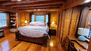 Un dormitorio de cabaña de madera con una cama grande, dos lámparas de noche, un calentador y un aparador de madera.