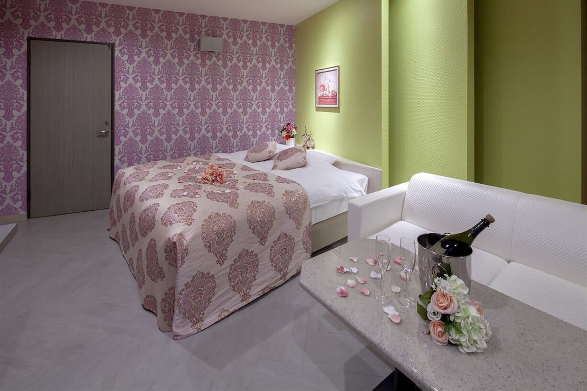 A bedroom with a bed, a white sofa, and a table with a bottle and flowers.