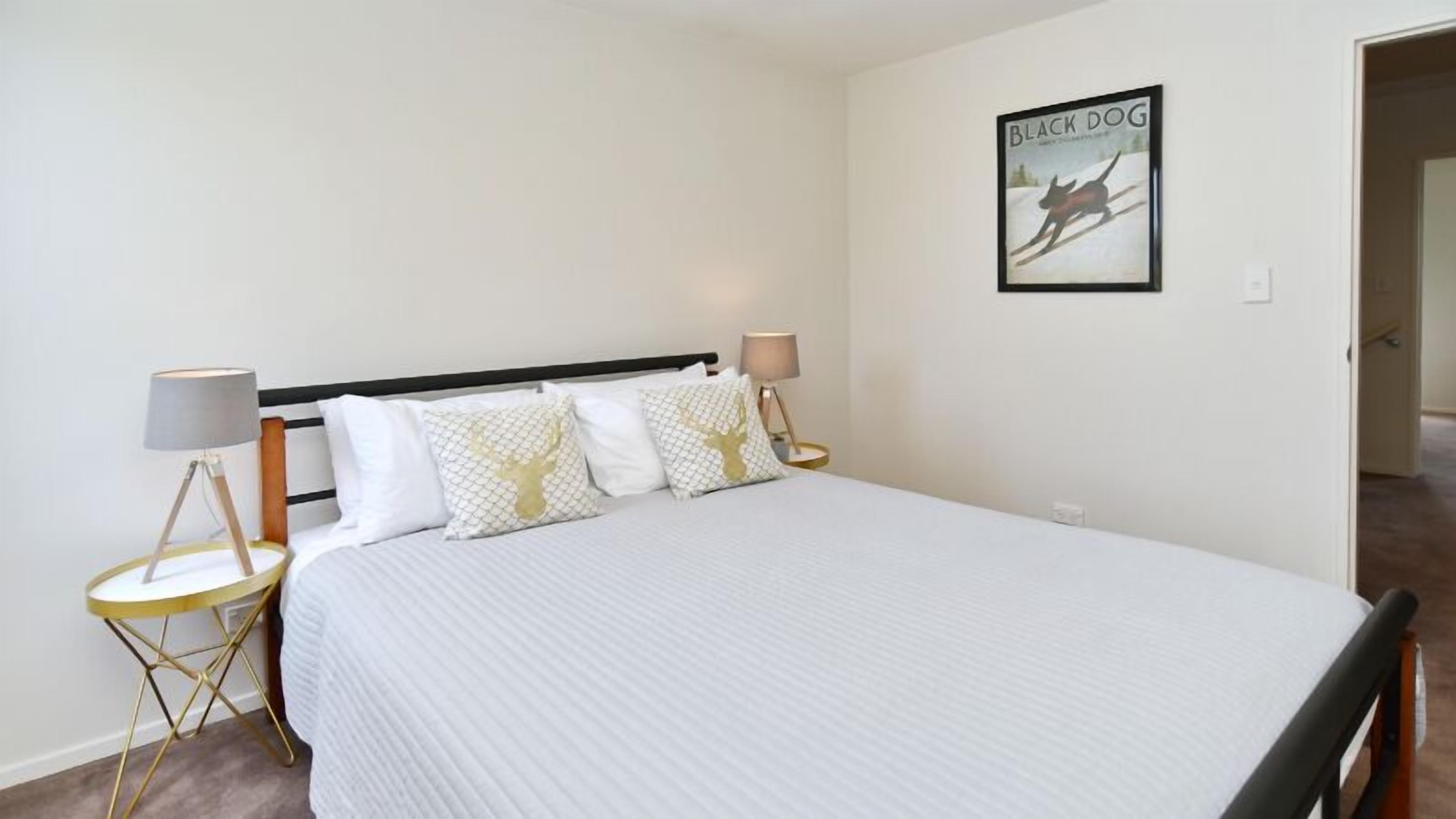 A bedroom with a bed, two bedside tables, a lamp, and a framed picture on the wall.