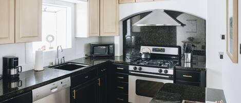 Una cocina moderna con armarios blancos y negros, un lavavajillas de acero inoxidable, una estufa a gas y un microondas.