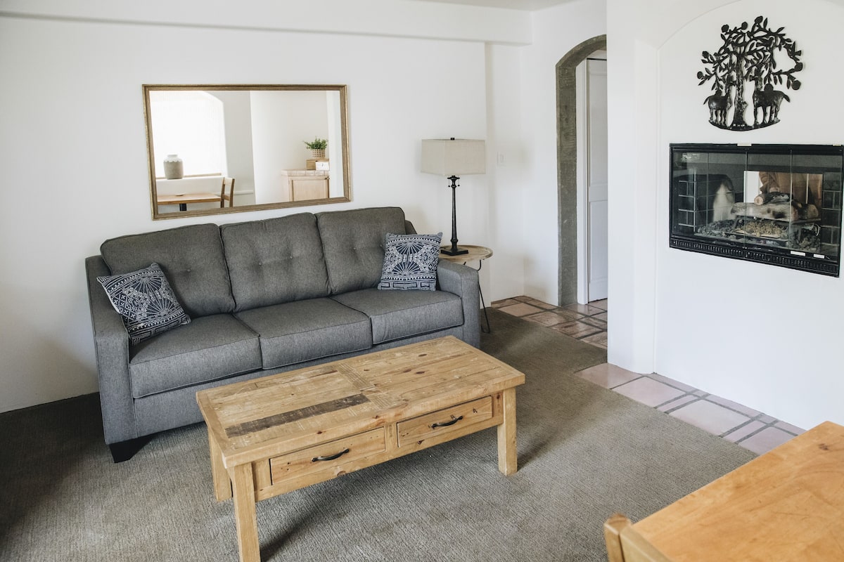 A living room with a grey sofa, a wooden coffee table, a lamp, and a wall-mounted TV.