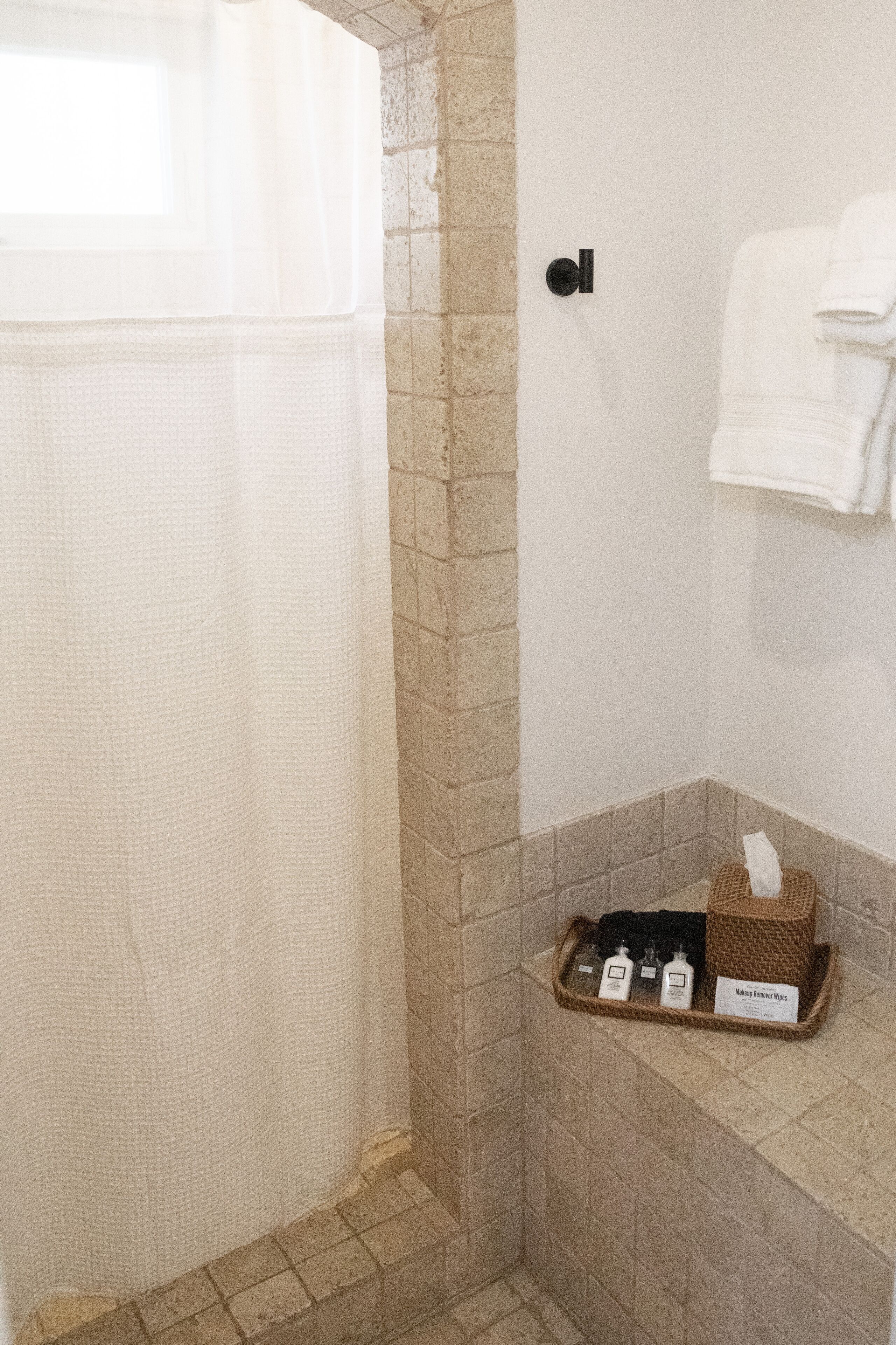 A bathroom with a shower curtain, a towel rack, and a shelf with toiletries.
