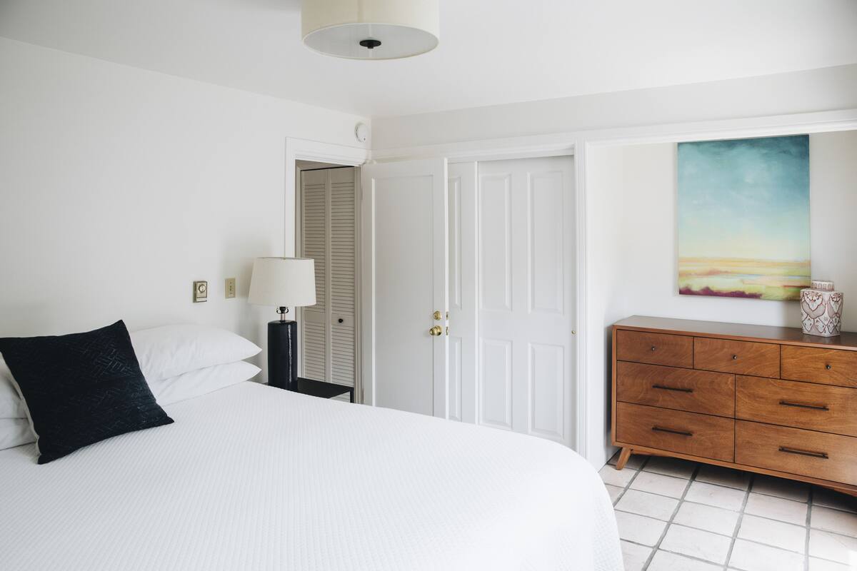 A bedroom with a large bed, a dresser, a nightstand, and a painting on the wall.