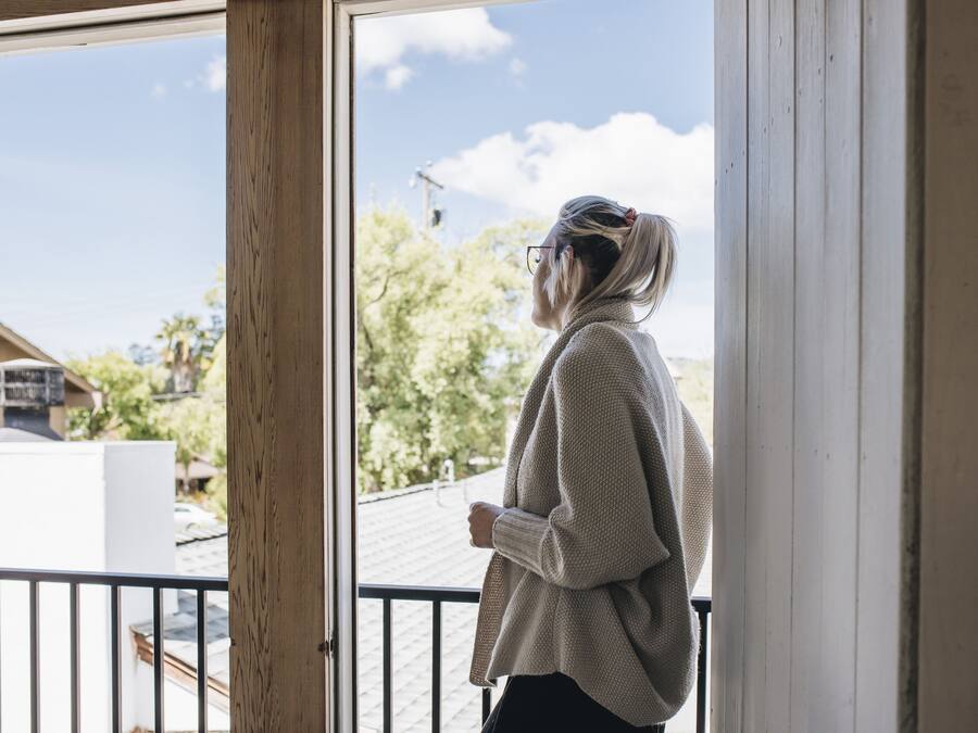 A person standing by a window with a view of trees and a building outside.