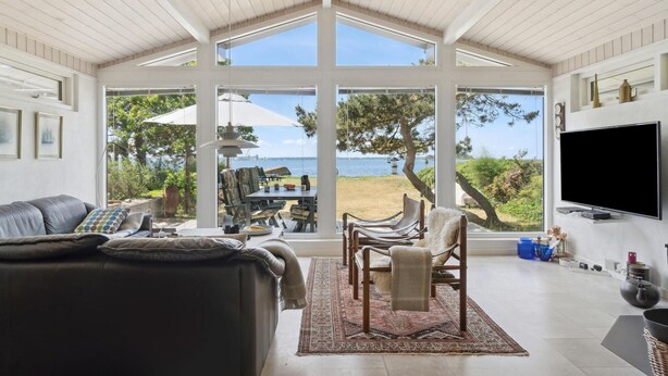 A spacious living area with a large window overlooking a beach, a leather sofa, a dining table, and a flat-screen TV mounted on the wall. - Beautiful home in Vordingborg with WiFi (Vordingborg)