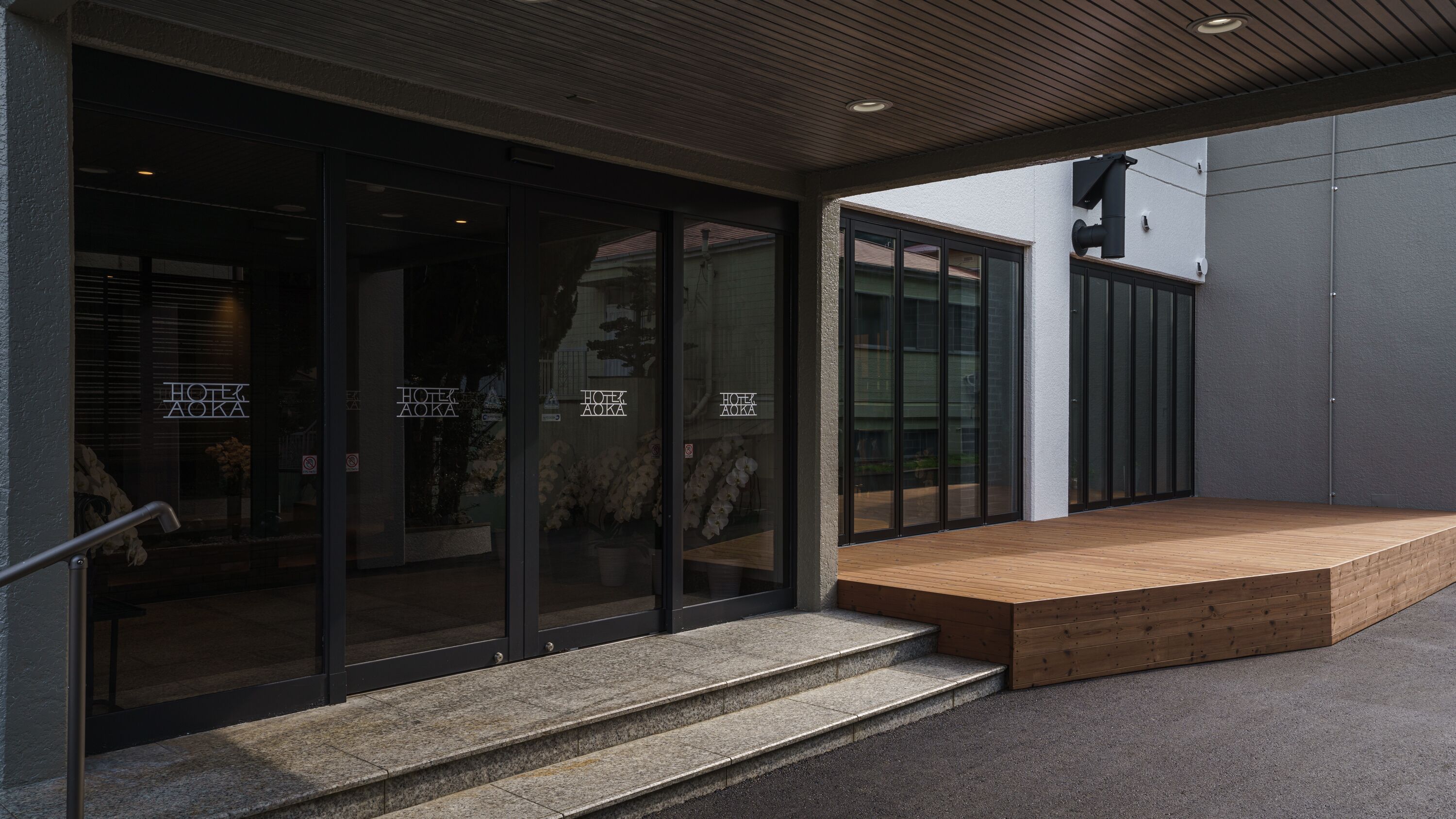 A modern hotel entrance with glass doors, a wooden bench outside, and a stone staircase leading up.